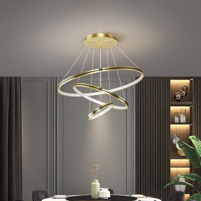 Gold Arisha three-ring pendant light above a round dining table beside a slatted wall