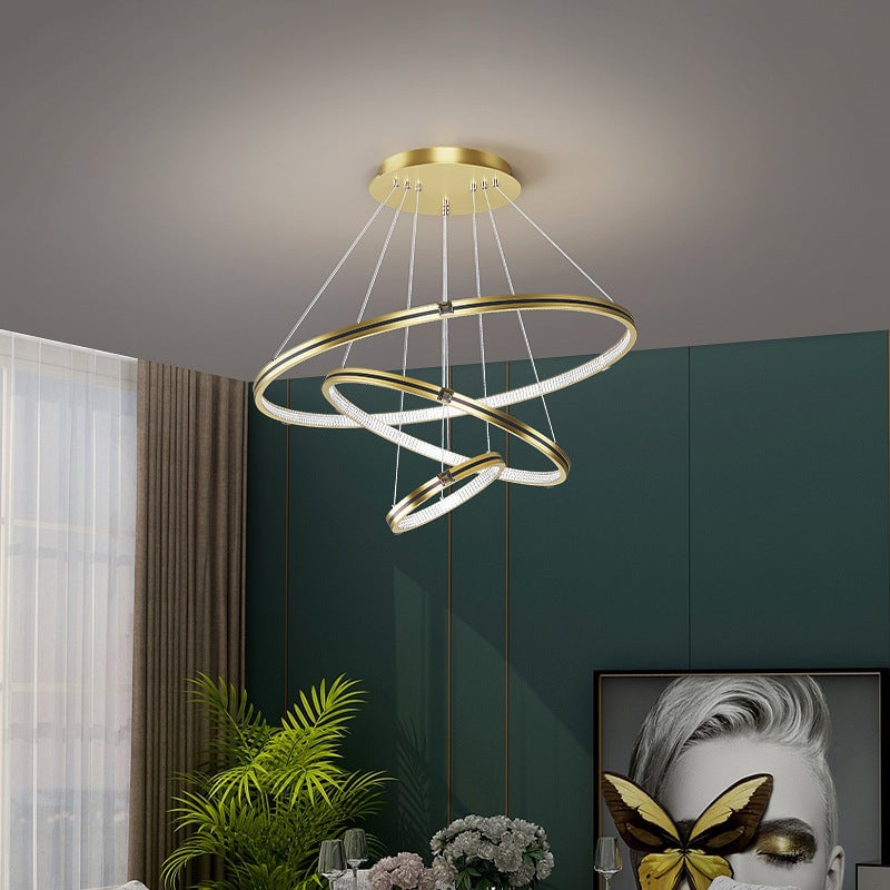Gold Arisha pendant light with three tilted rings in a room with a plant and wall artwork