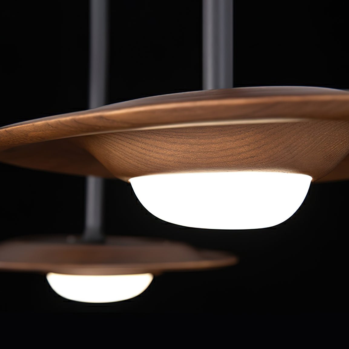 Close-up of a dark wood-grain curved shade and glowing white dome against black, with a second pendant behind