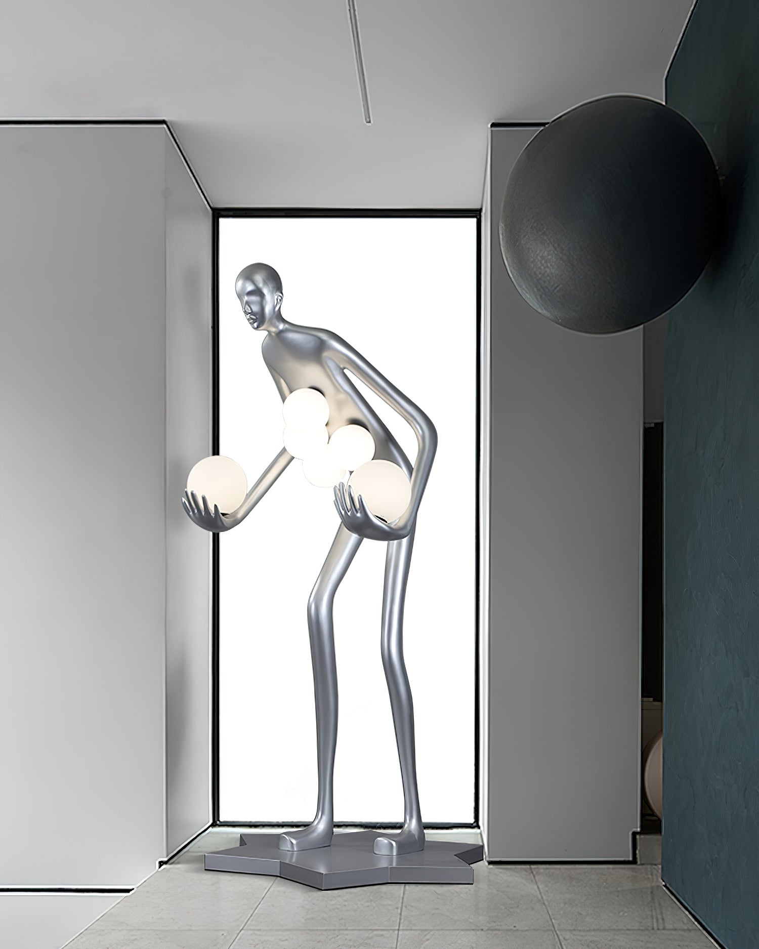 Wide view of a silver figure lamp by a tall window, with a dark round wall ornament and star base