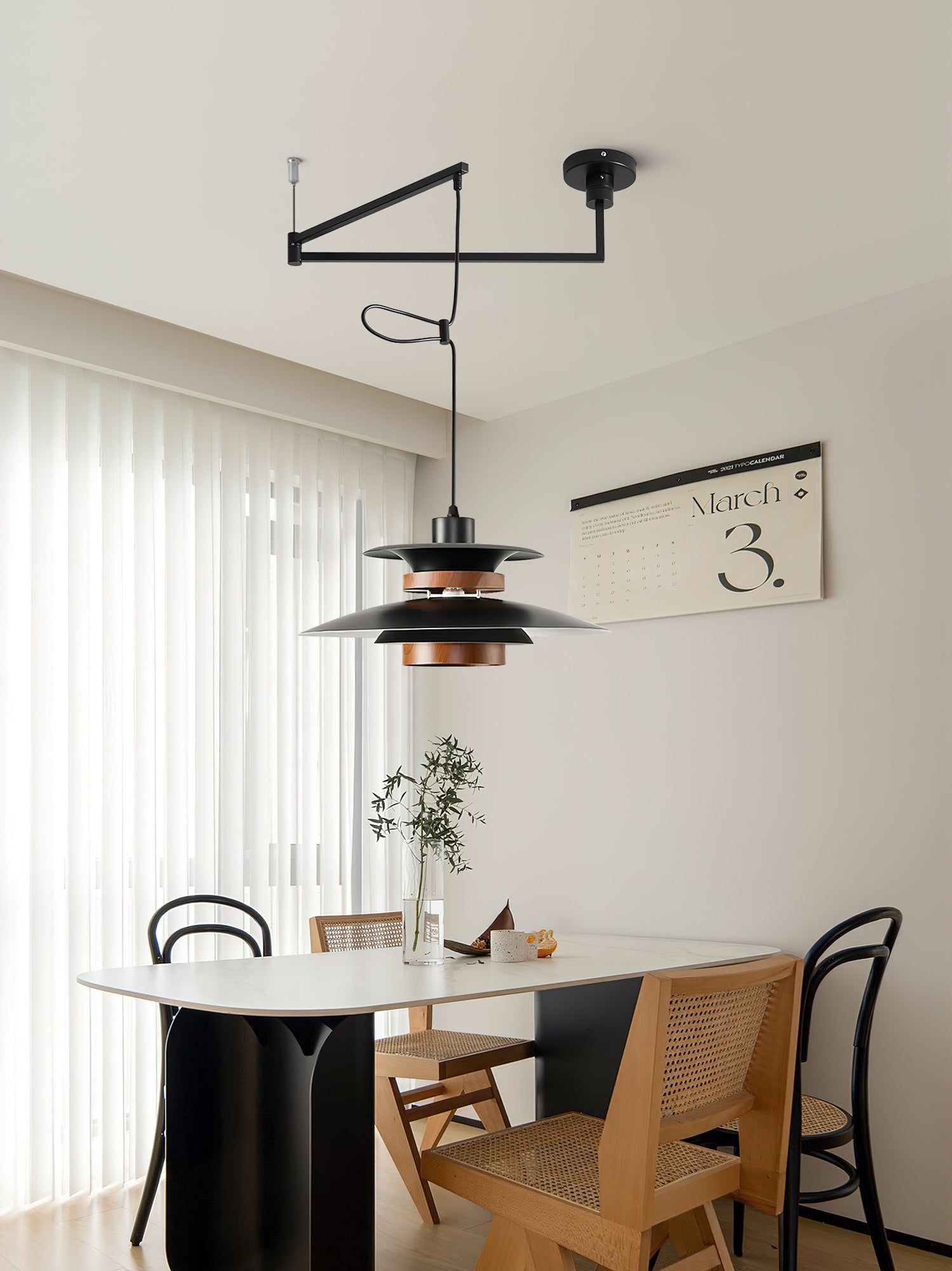 Mercero black layered pendant above a pale oval table with woven-back dining chairs