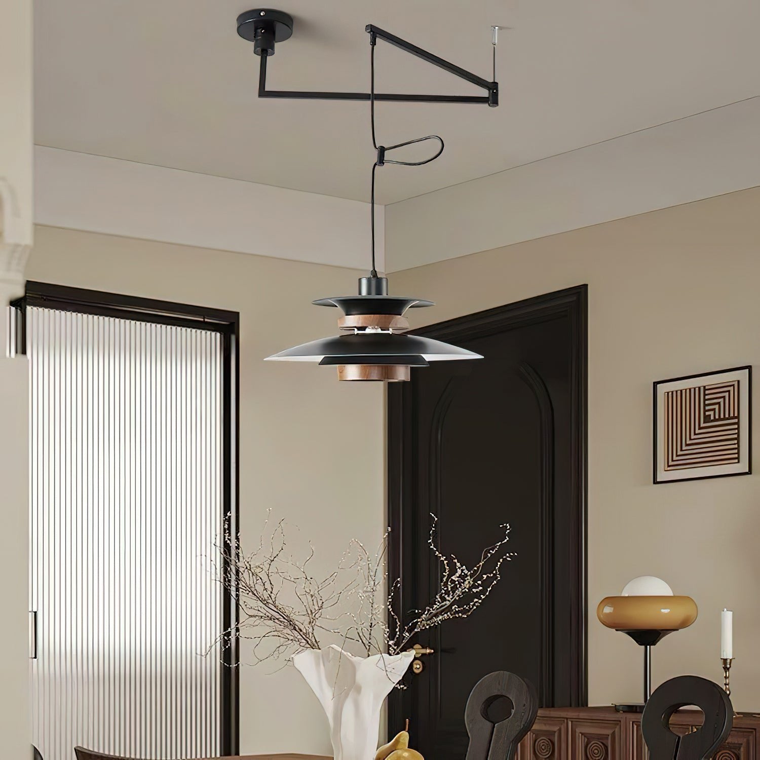 Black Mercero pendant and ceiling arm near a dark door and a white vase of branches
