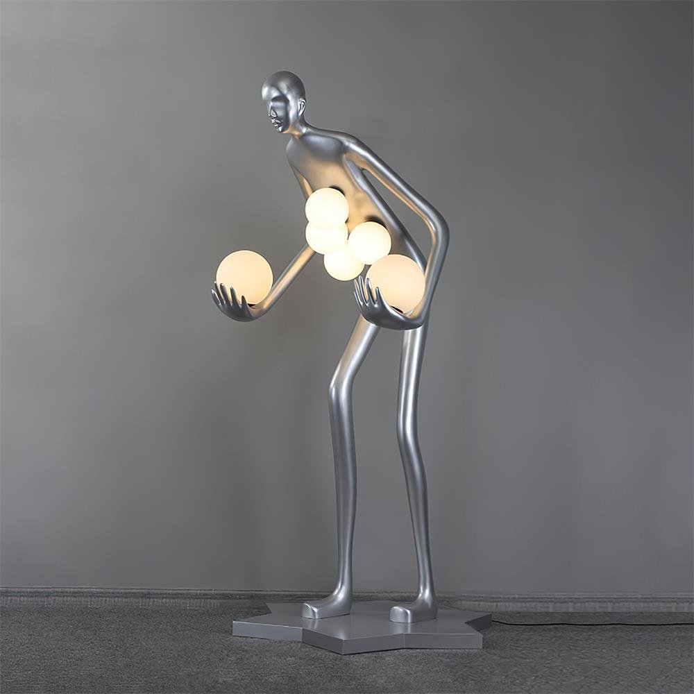 Silver human-figure lamp with six glowing white globes on gray carpet, with a cord to the right