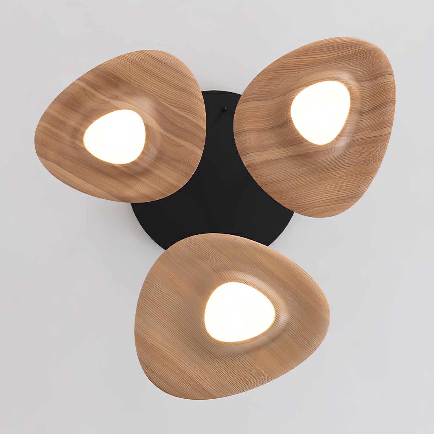 View from below of three light wood-grain disc shades around glowing white diffusers, with a black canopy behind