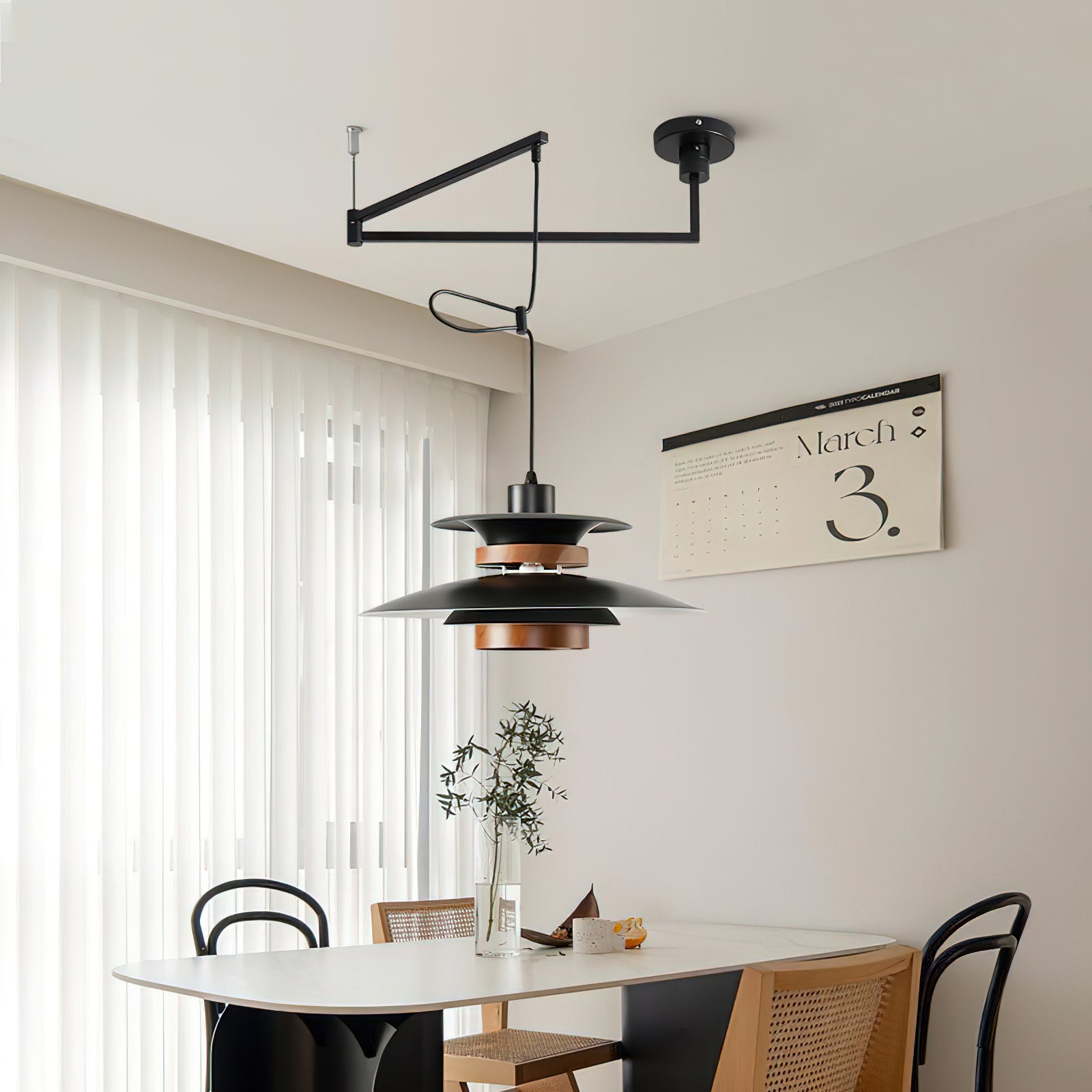 Black Mercero pendant and offset ceiling arm above an oval pale dining table beside sheer curtains