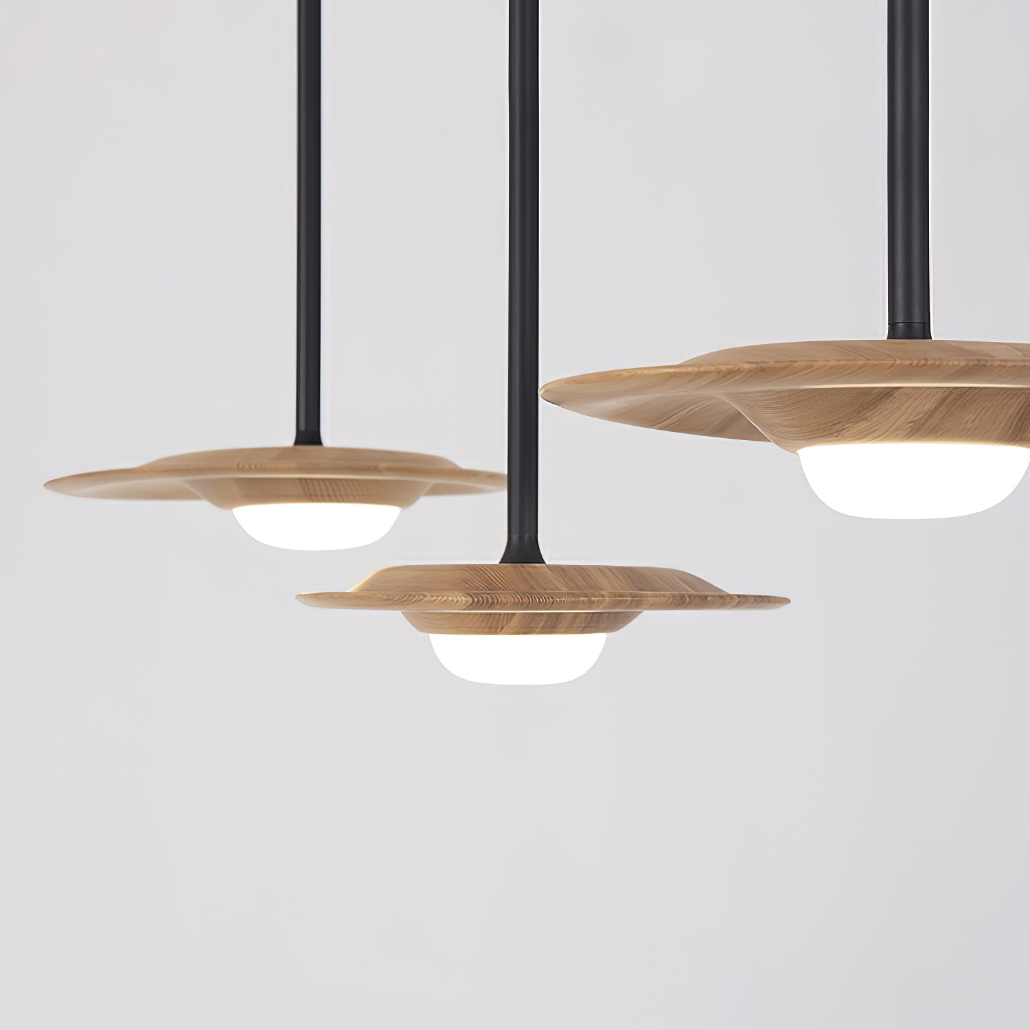 Close view of three light wood-grain disc shades, black rods and glowing white domed diffusers against grey
