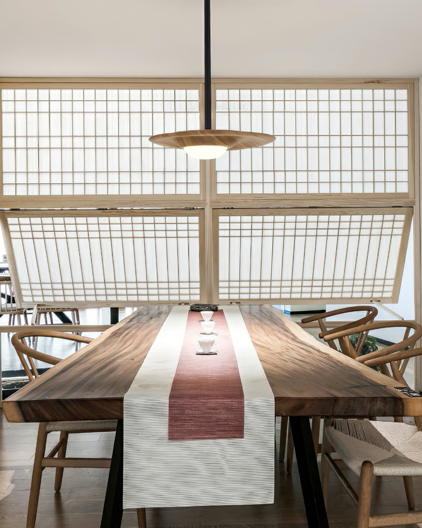 Single light wood-grain disc pendant over a wood tea table with cups and a runner, in front of pale lattice windows