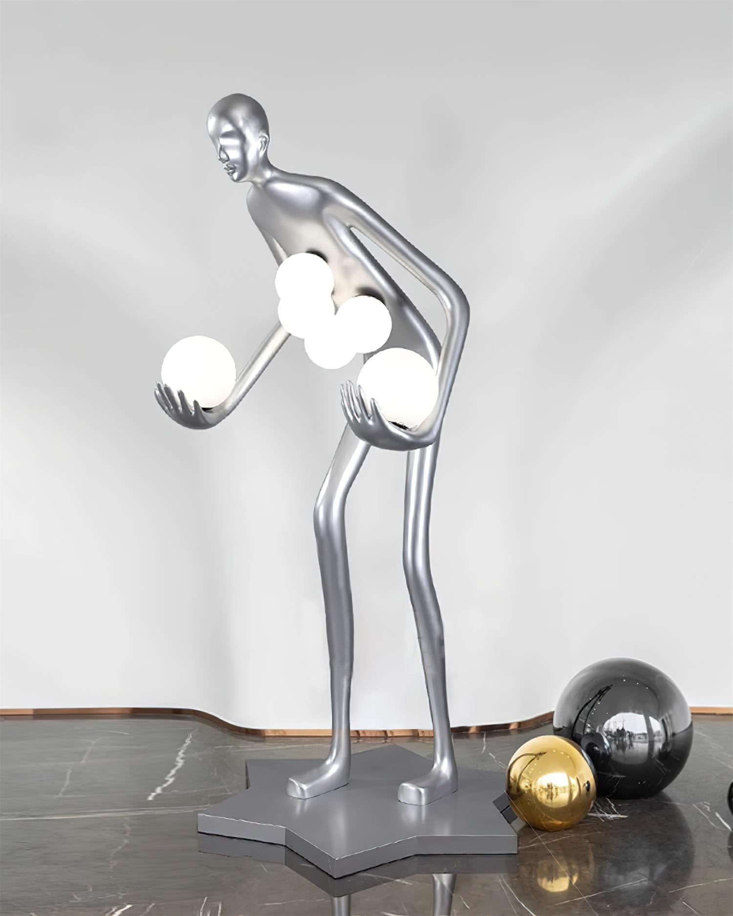 Silver figure with glowing white globes on marble, with separate gold-colored and black decorative balls nearby