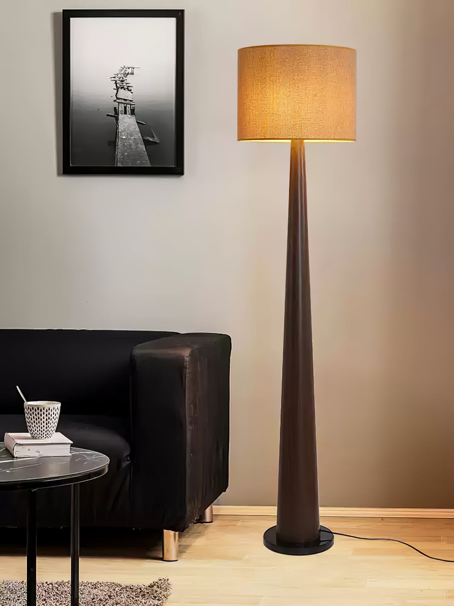 Dark brown floor lamp with textured beige drum shade beside a dark sofa and framed jetty photograph