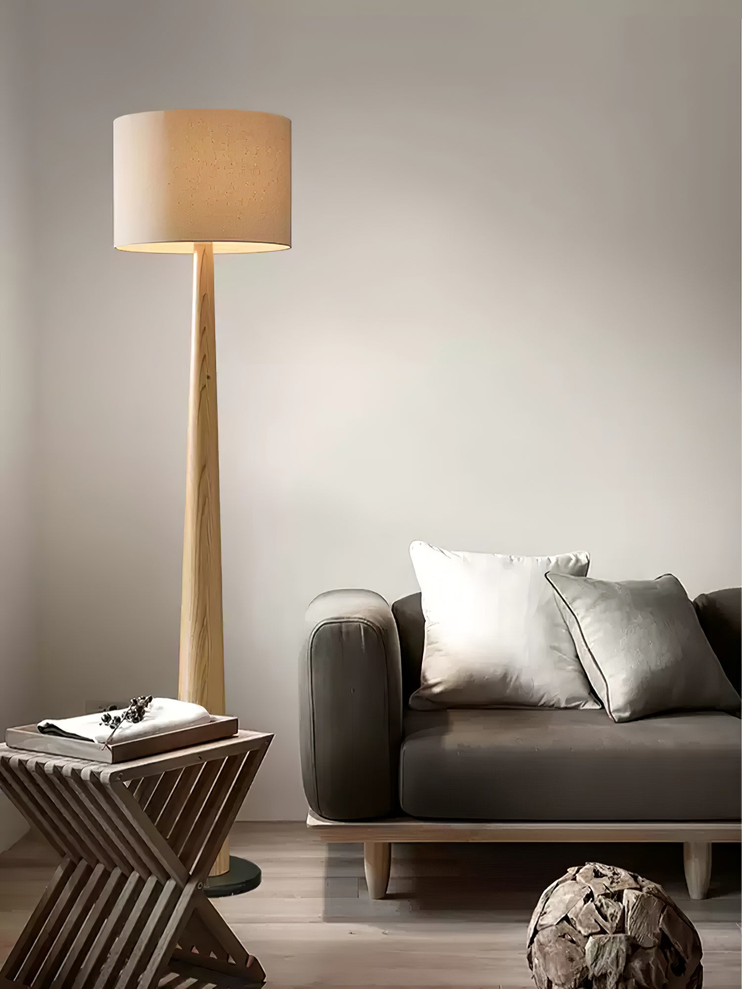 Light wood-tone floor lamp beside a gray sofa with pale cushions and a crossed-leg wooden side table