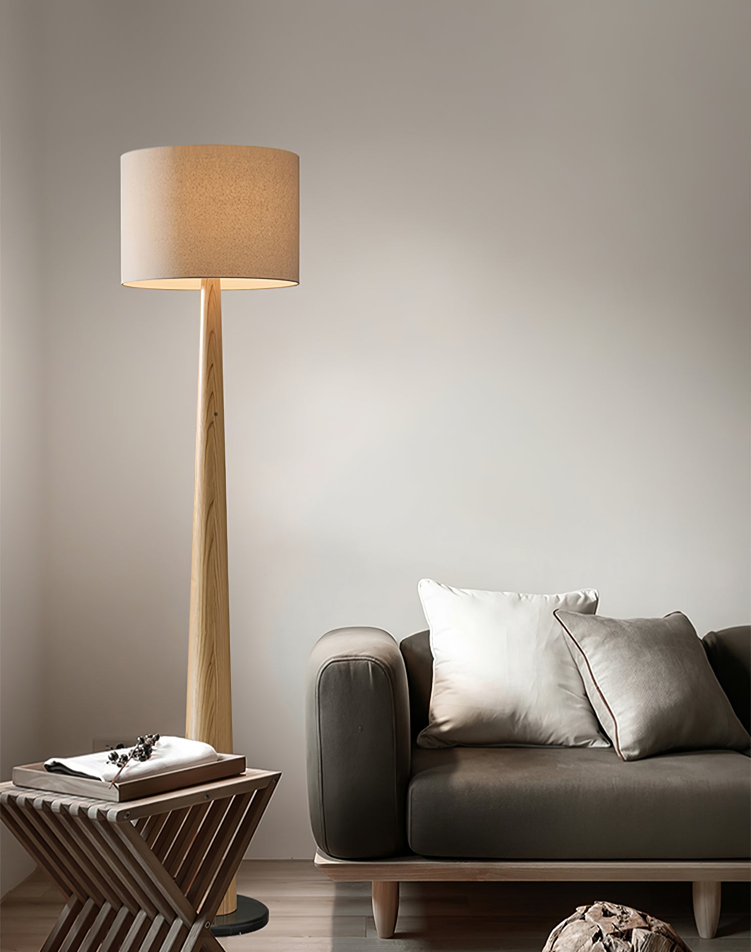 Light wood-grain floor lamp with drum shade beside a gray sofa, pale cushions and wooden side table