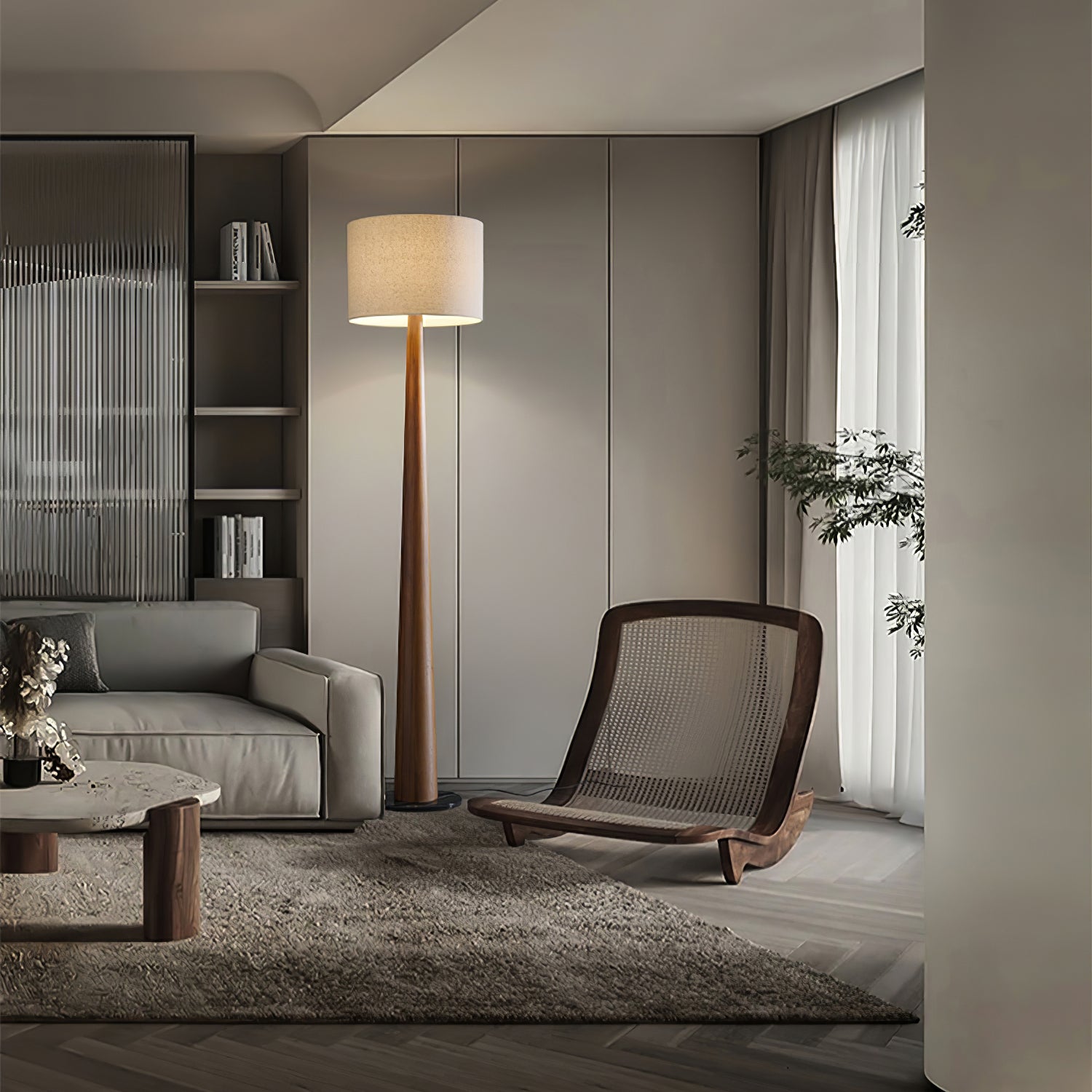 Tall wood-tone floor lamp with pale drum shade between a sofa and woven lounge chair in a gray-panelled room