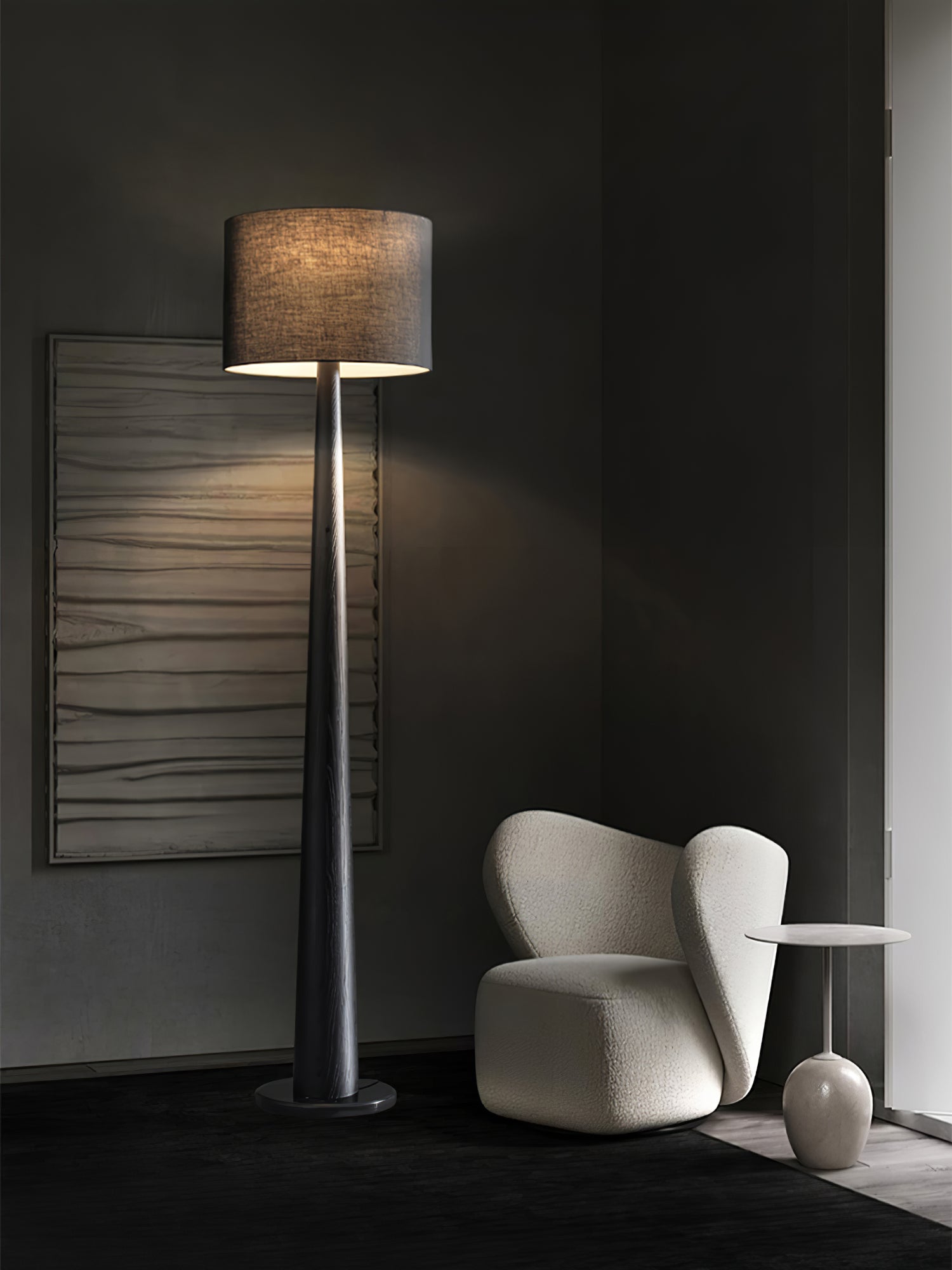 Black wood-grain floor lamp with illuminated dark shade beside a curved cream chair and white side table