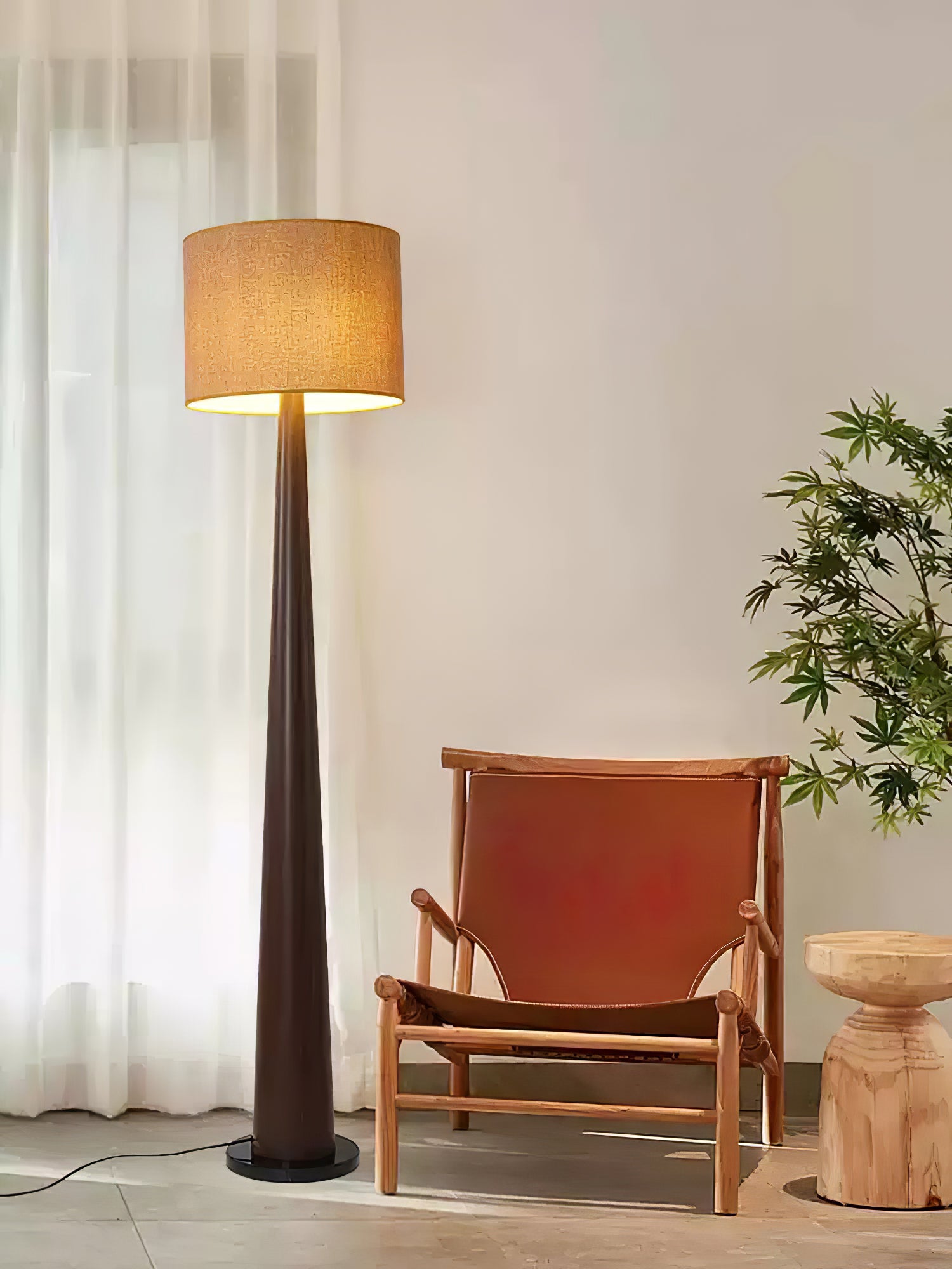 Dark brown tapered lamp with textured beige drum shade beside a leather sling chair and small wood table