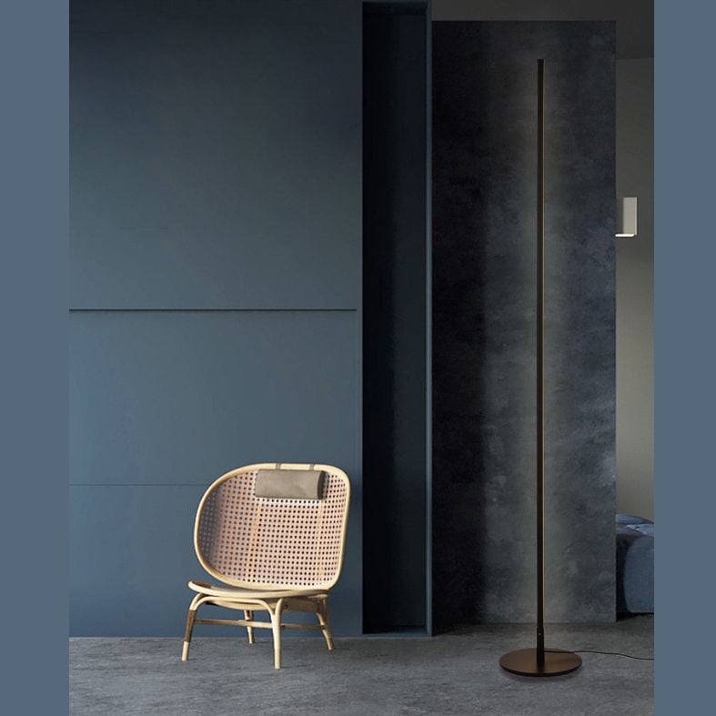 Edge floor lamp in a dark room beside a woven chair