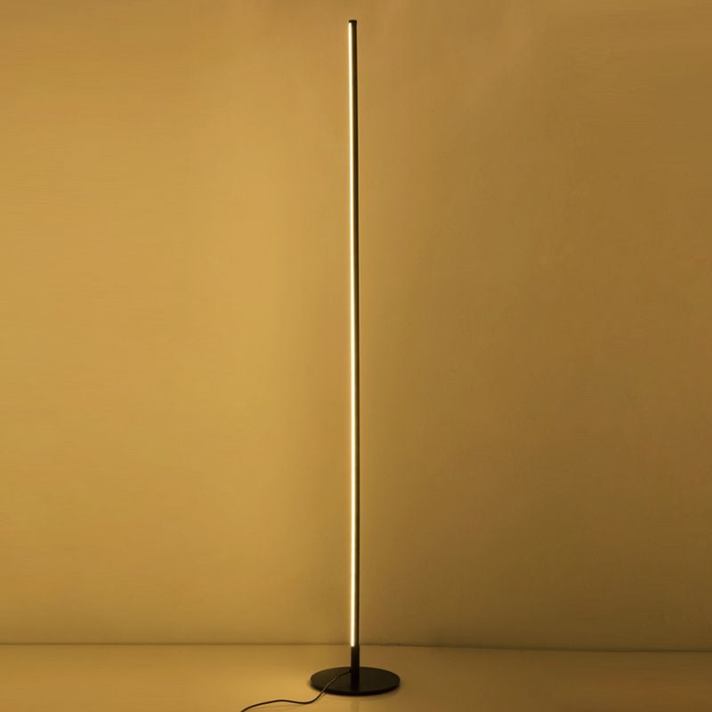 Gold-toned Edge floor lamp illuminated against a warm-coloured wall