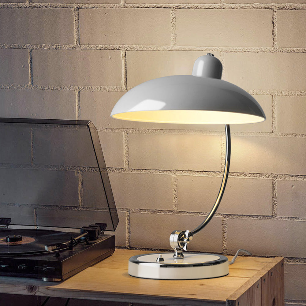 White dome table lamp with curved metal stem beside a record player on a wood cabinet against brickwork