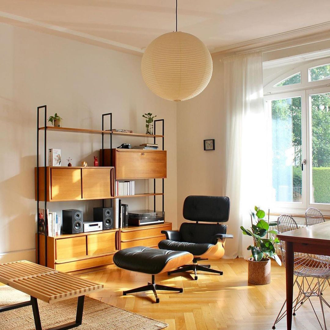 Paper globe above a black leather and wood lounge chair with footstool near a stereo shelf and window