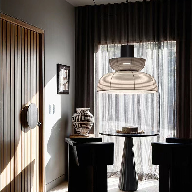 Small upper bowl and lower dome pendant above a round table beside dark curtains and a wooden door