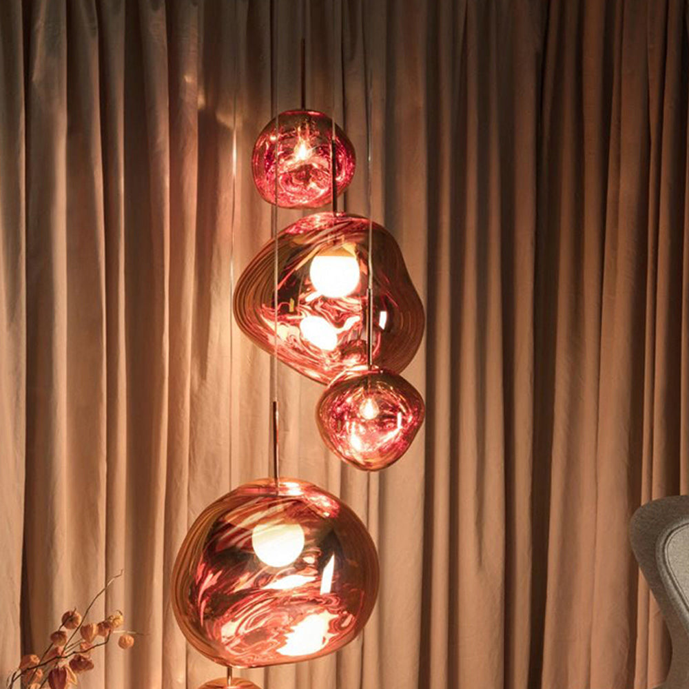 Four glowing Rose Gold irregular shades before bronze curtains, with grey upholstery and a dried branch below