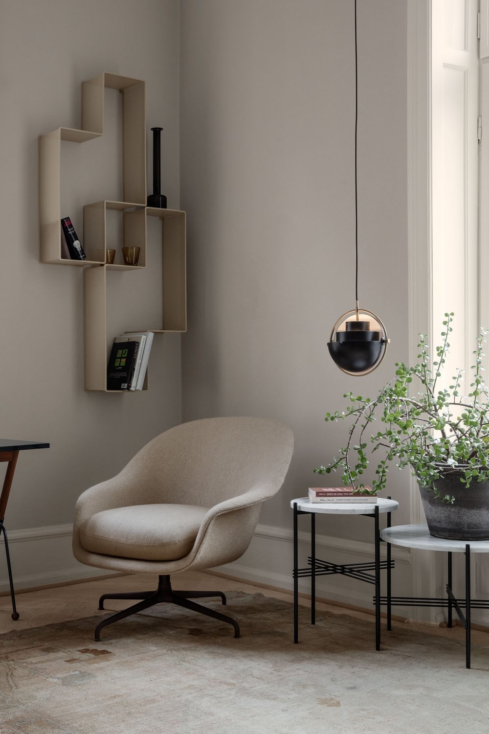 Reflective dark ring pendant beside a cream recliner and a small plant.
