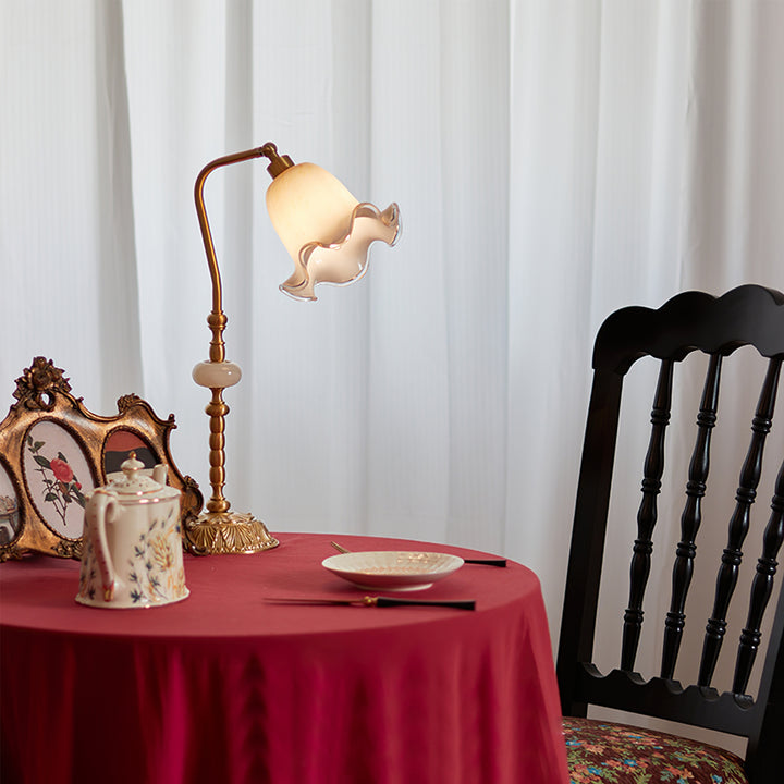 Lit flower-shade lamp on a red cloth-covered dining table beside floral teapot, plate and cutlery, near a black chair
