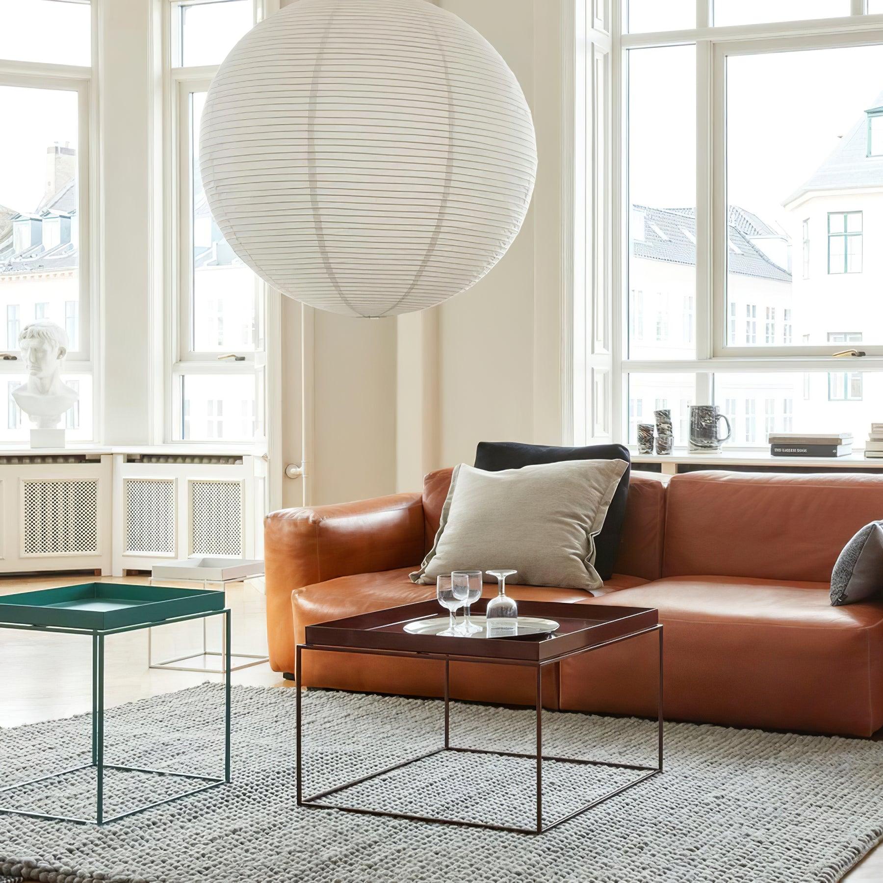 Large paper globe above a brown leather sofa with pale cushions and two square tray tables