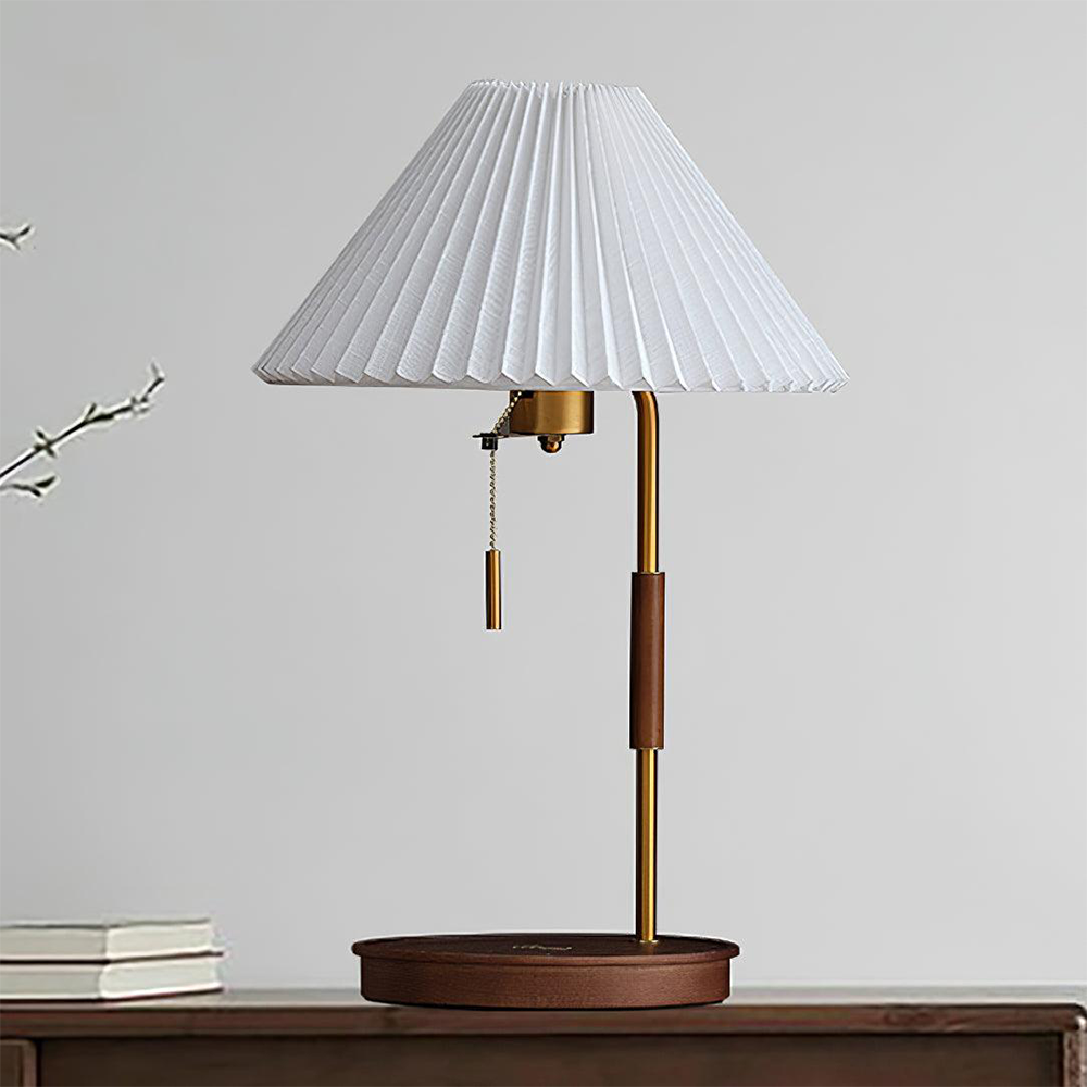 Unlit Walnut lamp with a pleated white shade and dark wood base on a wood cabinet beside books