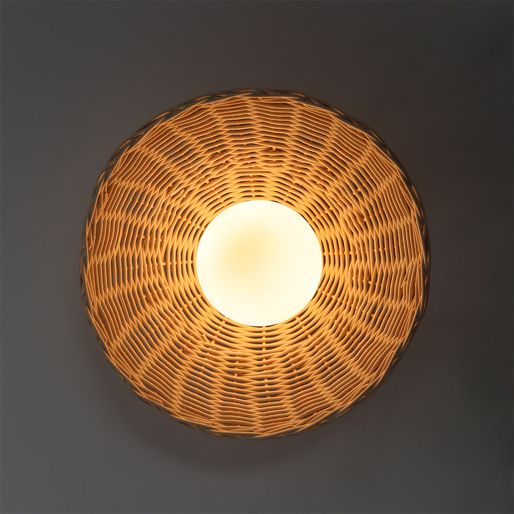 Front view of lit woven circular shade and bright globe against a dark grey wall