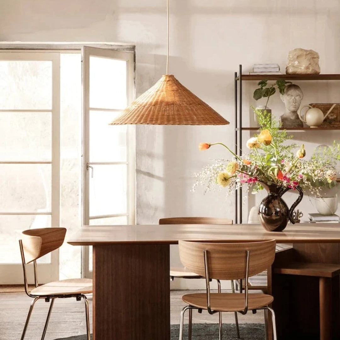 Natural-tone woven cone pendant above a wooden dining table with flowers beside pale open windows