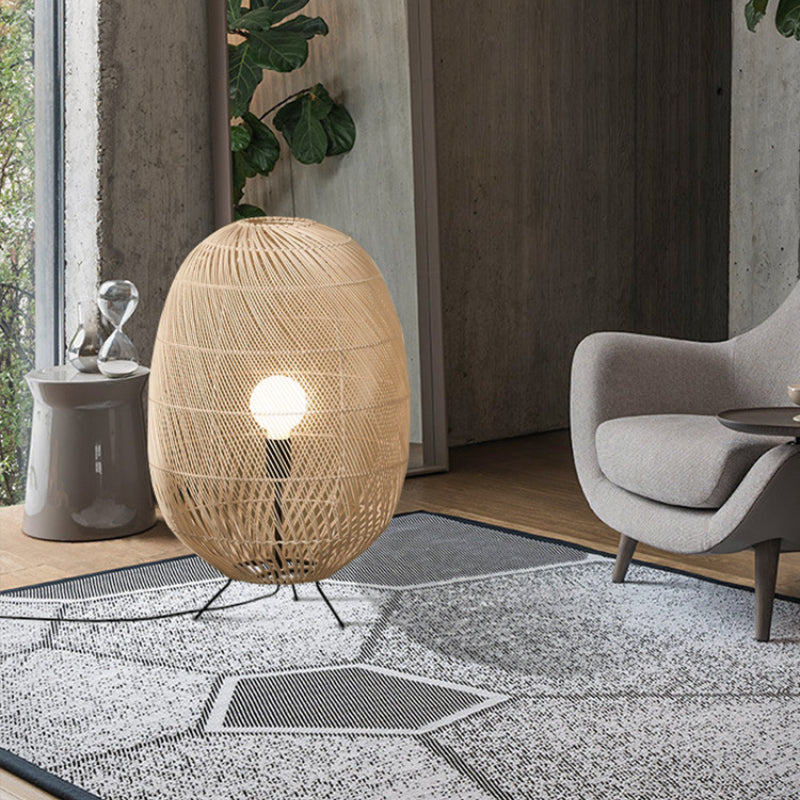 Glowing rattan lamp on geometric rug beside a grey armchair, window and hourglass-shaped side table