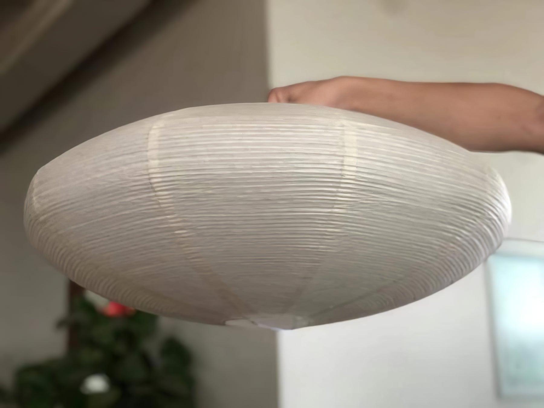 Hand holding a flattened White paper shade with visible ribs, joins and bottom opening