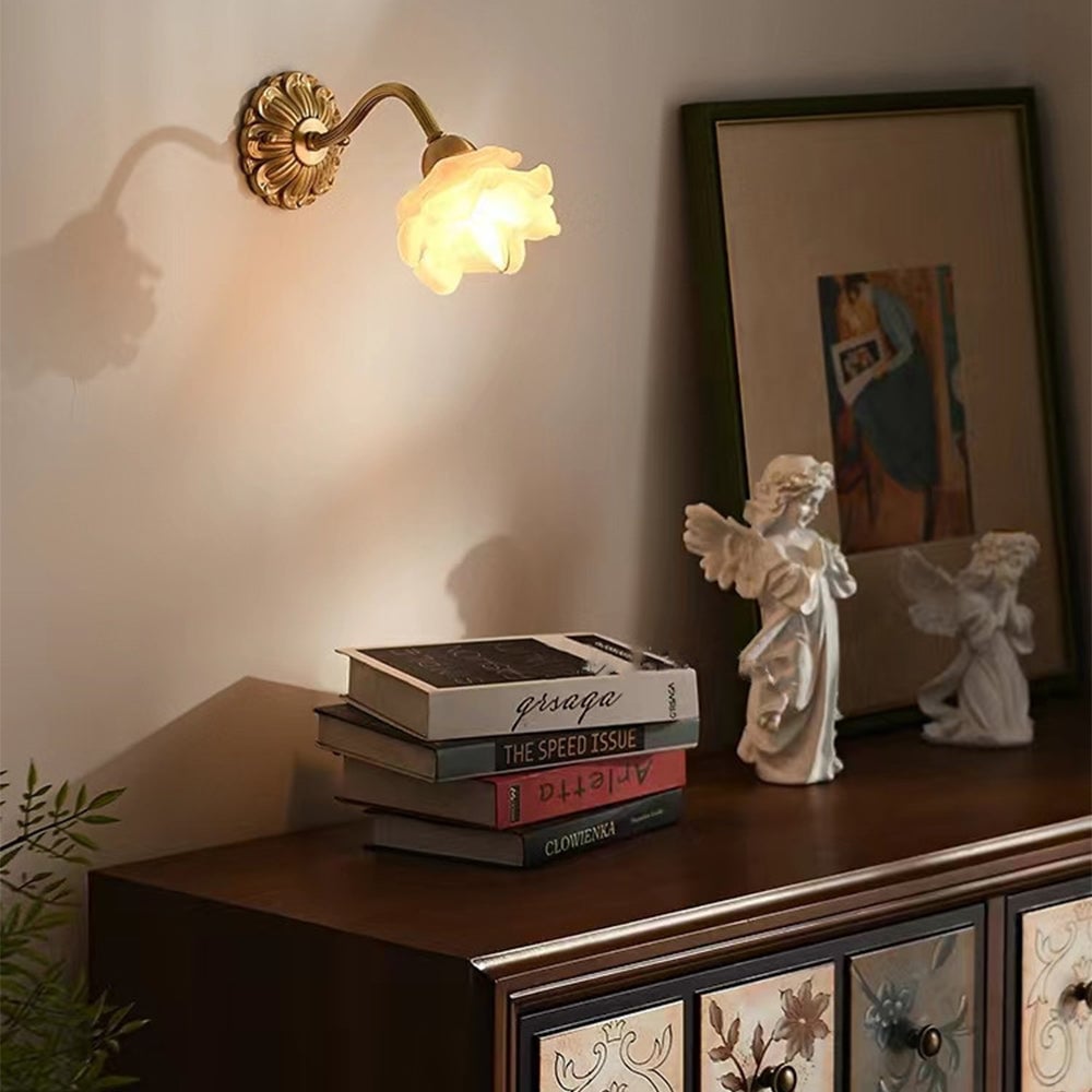 Lit flower wall light above books and angel figures on a cabinet with floral drawer fronts