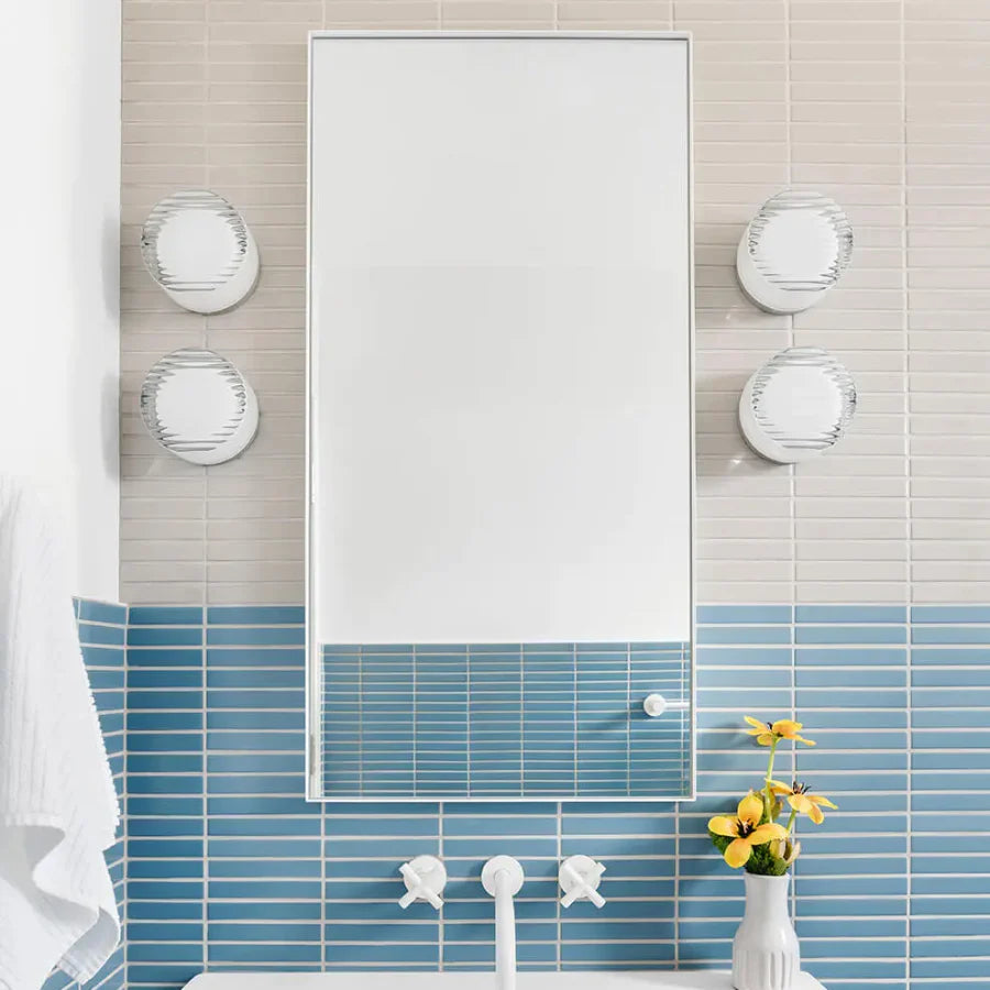 Four white round lights beside a bathroom mirror over blue-and-cream tiles, white taps and a flower vase
