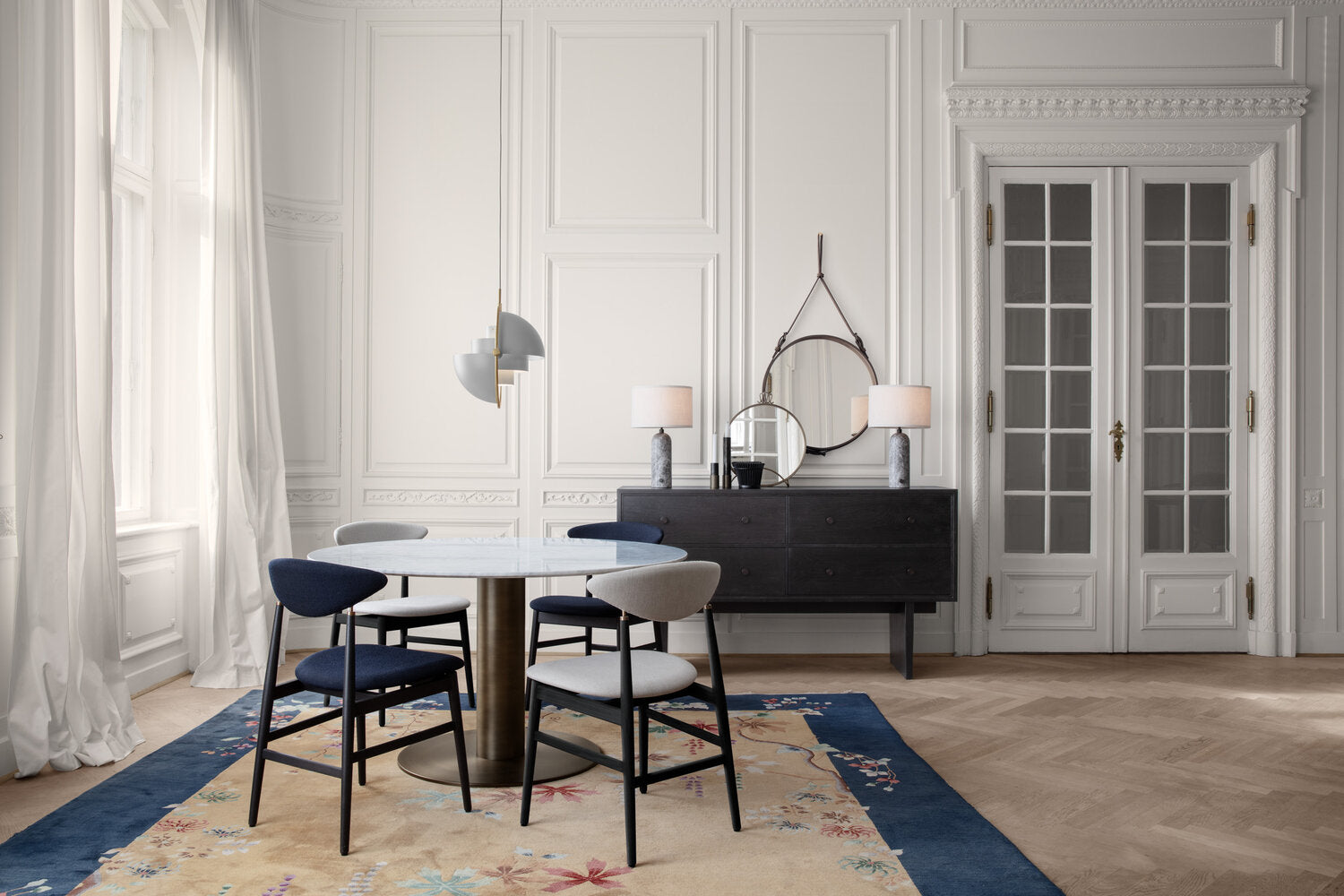 Two pale adjustable pendants above a round dining table in a white room.