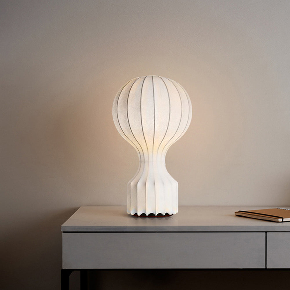 Illuminated white ribbed lamp with a scalloped lower edge on a grey desk beside a notebook