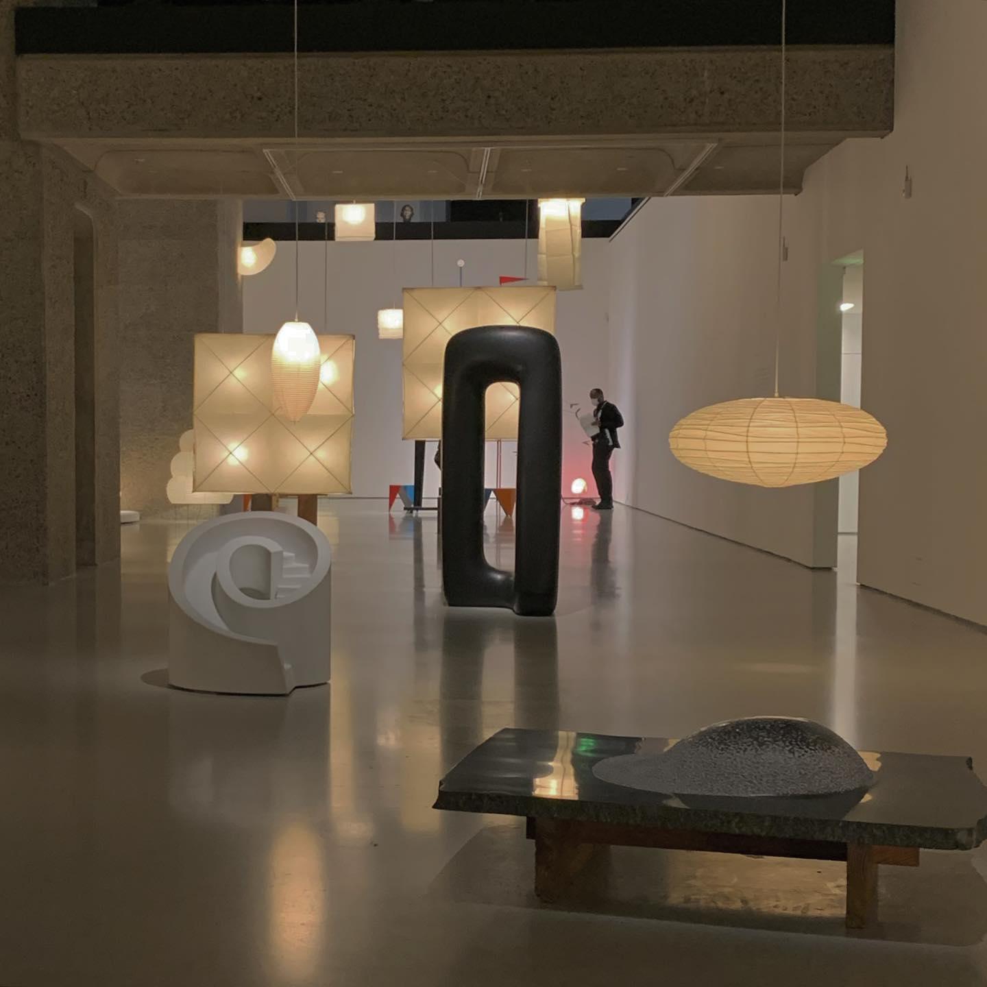 Flattened glowing paper shade in an exhibition hall with square lights and black and white sculptures