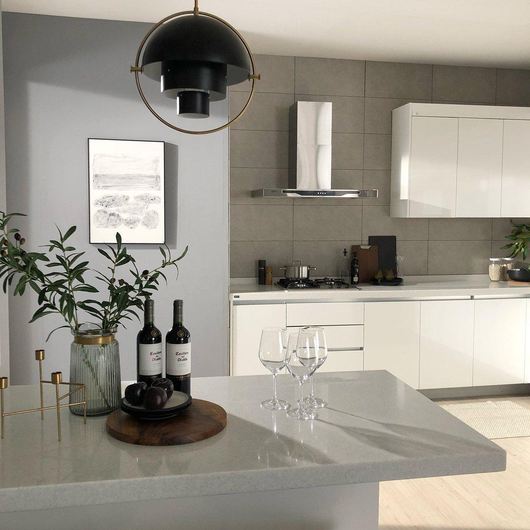 Black circular-frame pendant over a kitchen counter with plants and glassware.