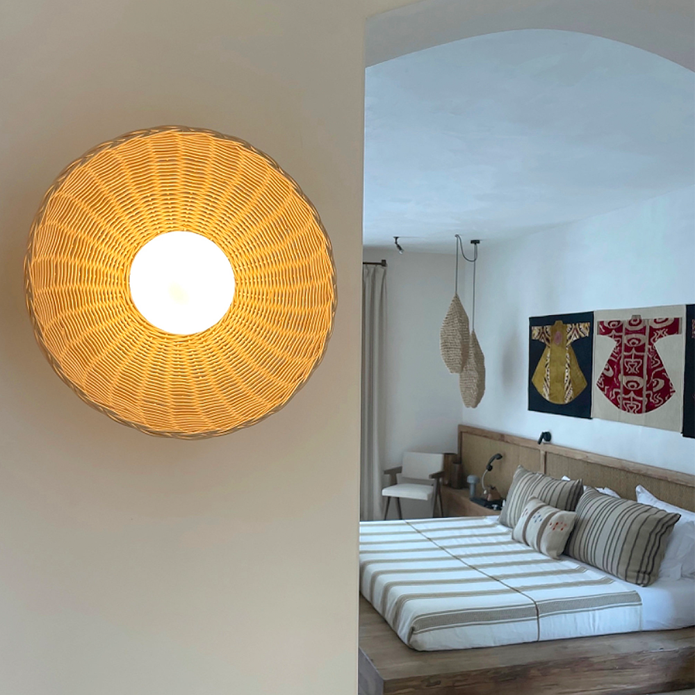 Lit pale woven wall light beside a bedroom doorway, with wood bed and striped white bedding beyond