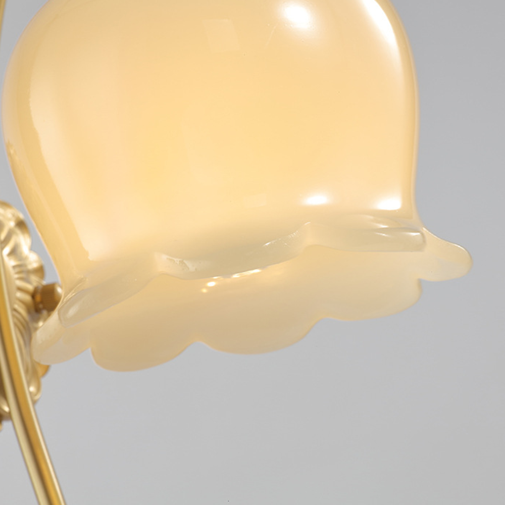 Close-up of lit milky-white glass shade with flared scalloped rim and partial gold-tone arm