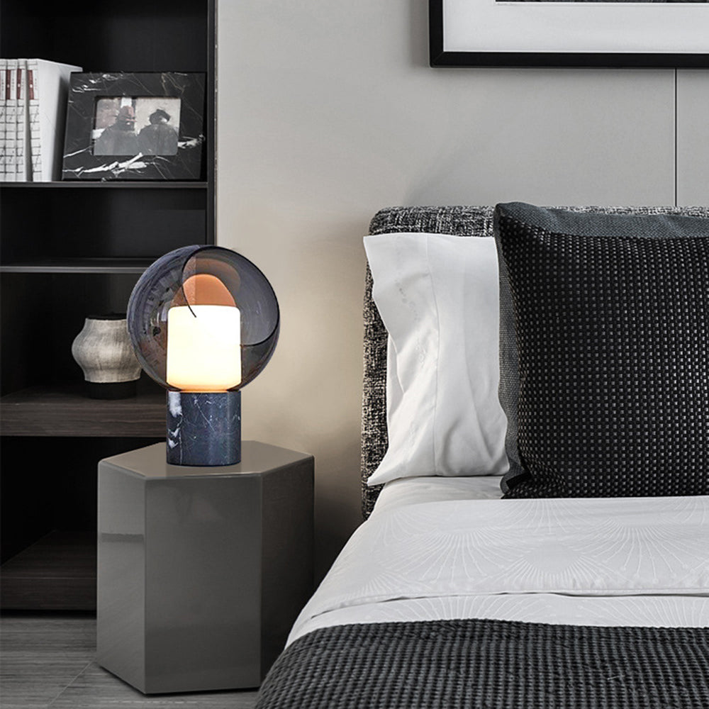 Lit smoky glass and dark veined base on a faceted grey bedside pedestal beside black-and-white bedding