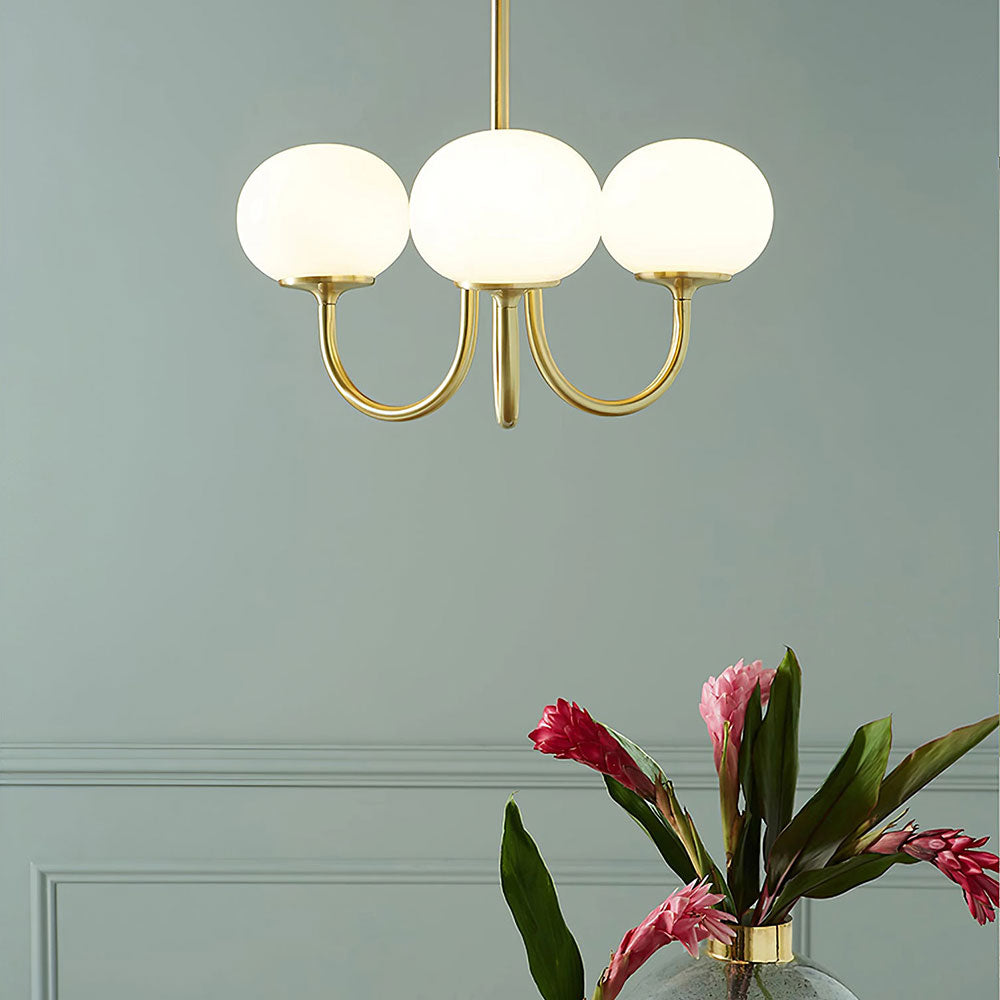 Three illuminated white globes on gold-tone arms against a green wall with flowers below