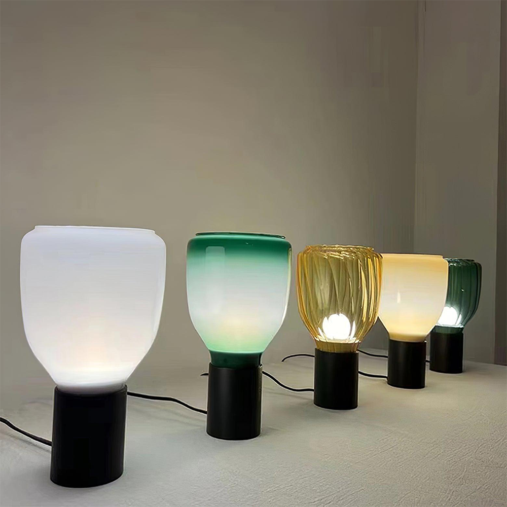 Angled view of five tall glass lamps with black cylindrical bases and trailing cords on a pale tabletop