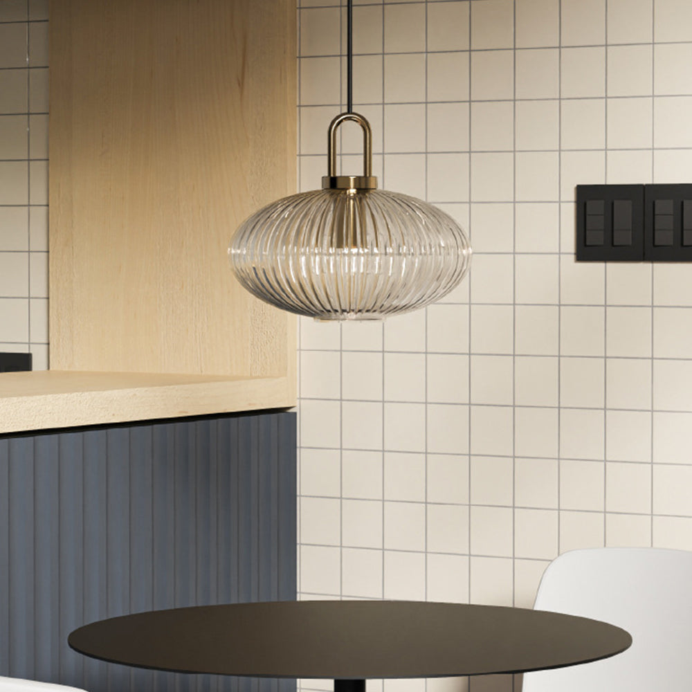 Wide flattened clear ribbed glass pendant above a dark round table beside a tiled wall