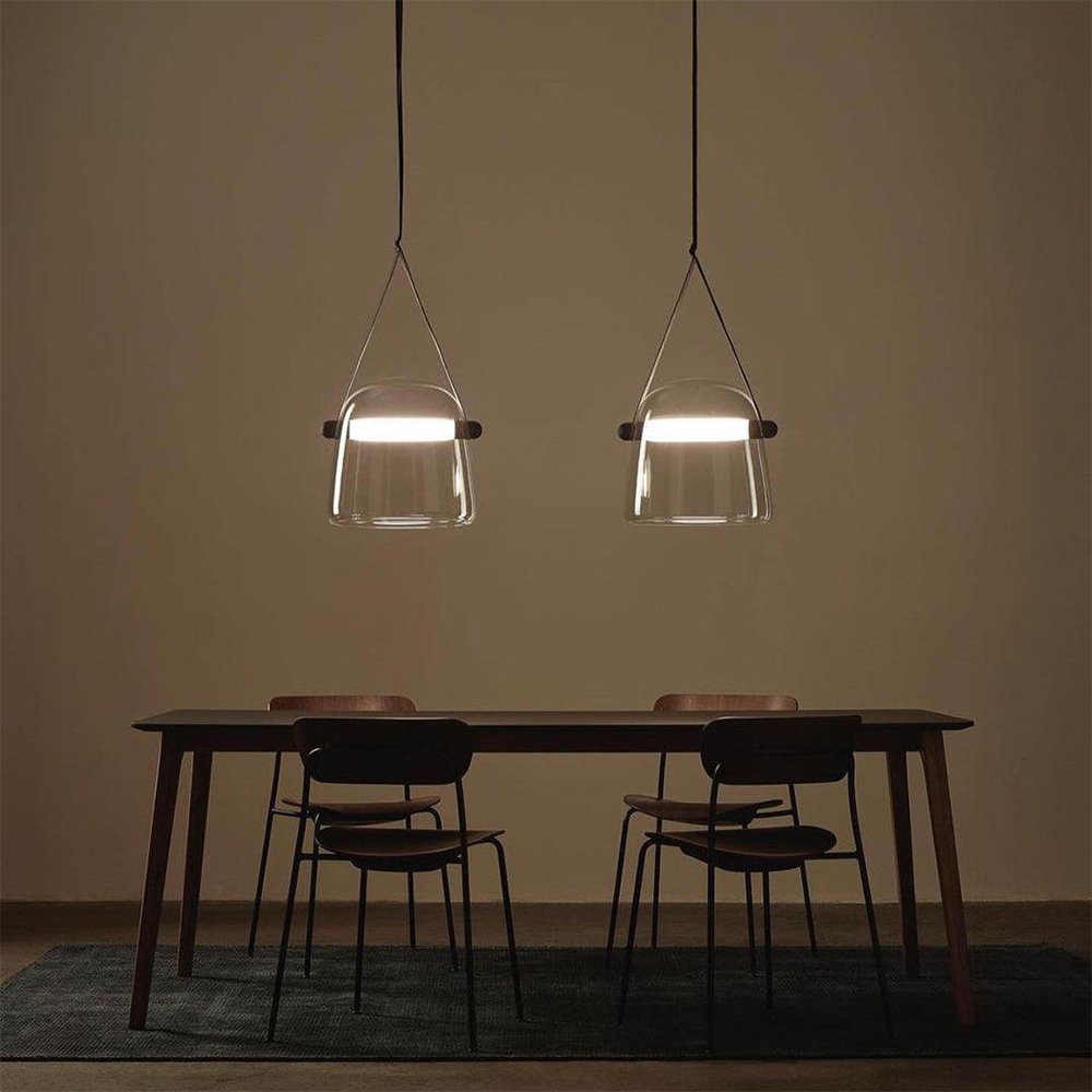 Two clear-looking glass pendants with dark split straps and bright bars above a rectangular dining table
