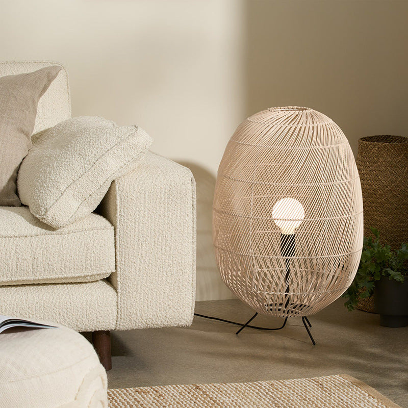 Woven oval lamp beside ivory sofa and cushions, cream-and-rust rug and pale ottoman with open book