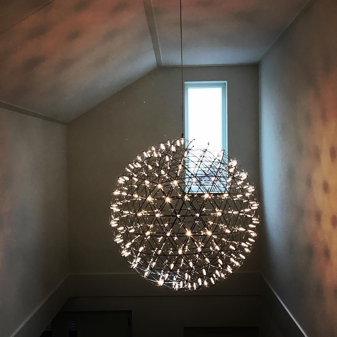 Silver globe pendant hanging in a tall stairwell near a sloping ceiling and narrow window