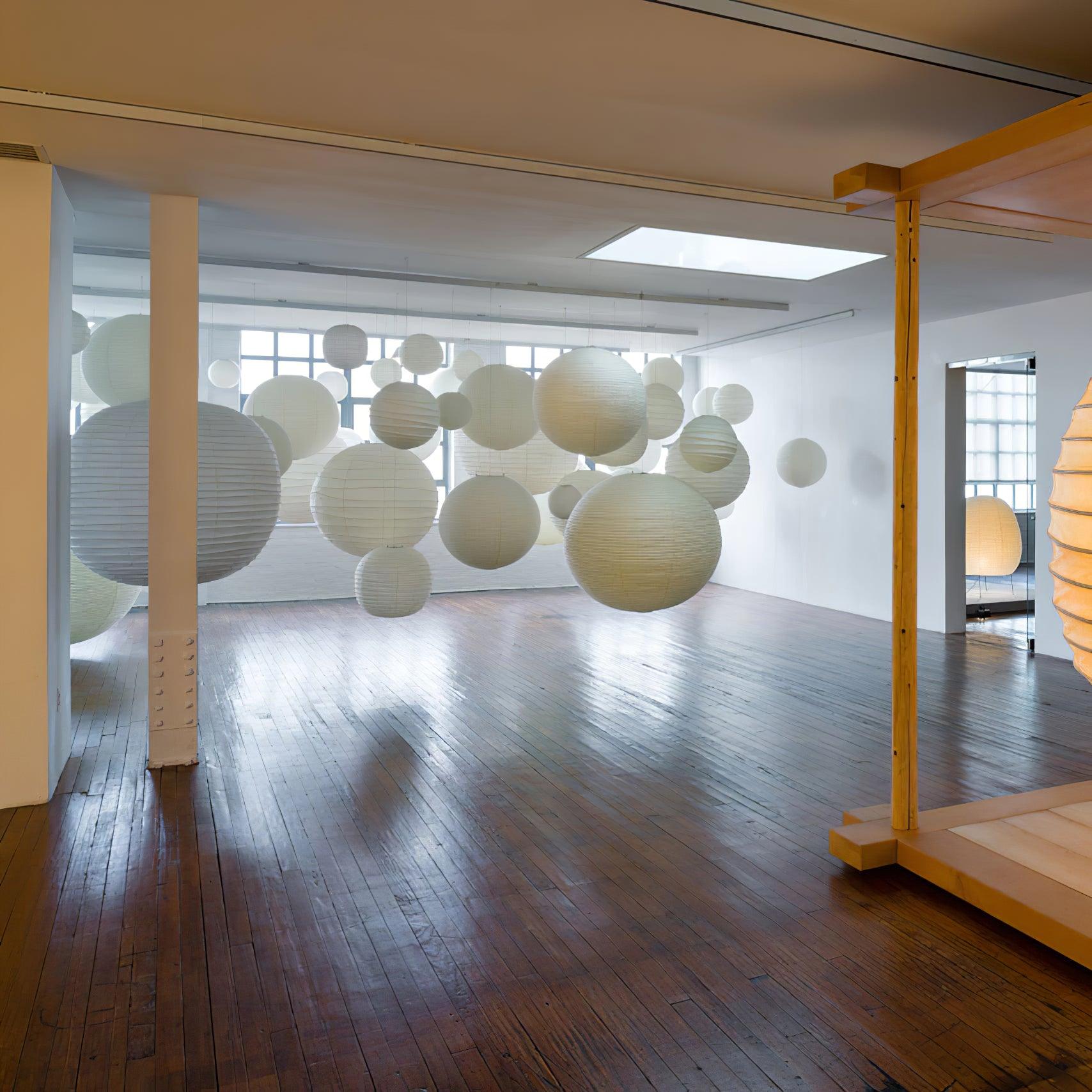 Globe paper shades of different sizes beneath a showroom skylight with white columns and wooden floor