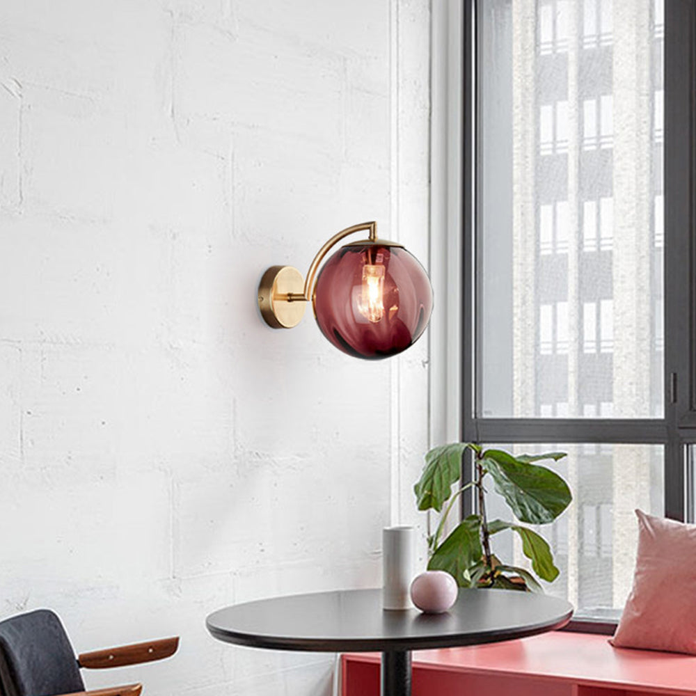 Red glass globe lamp by a window above black round table, with green plant and pink bench seating