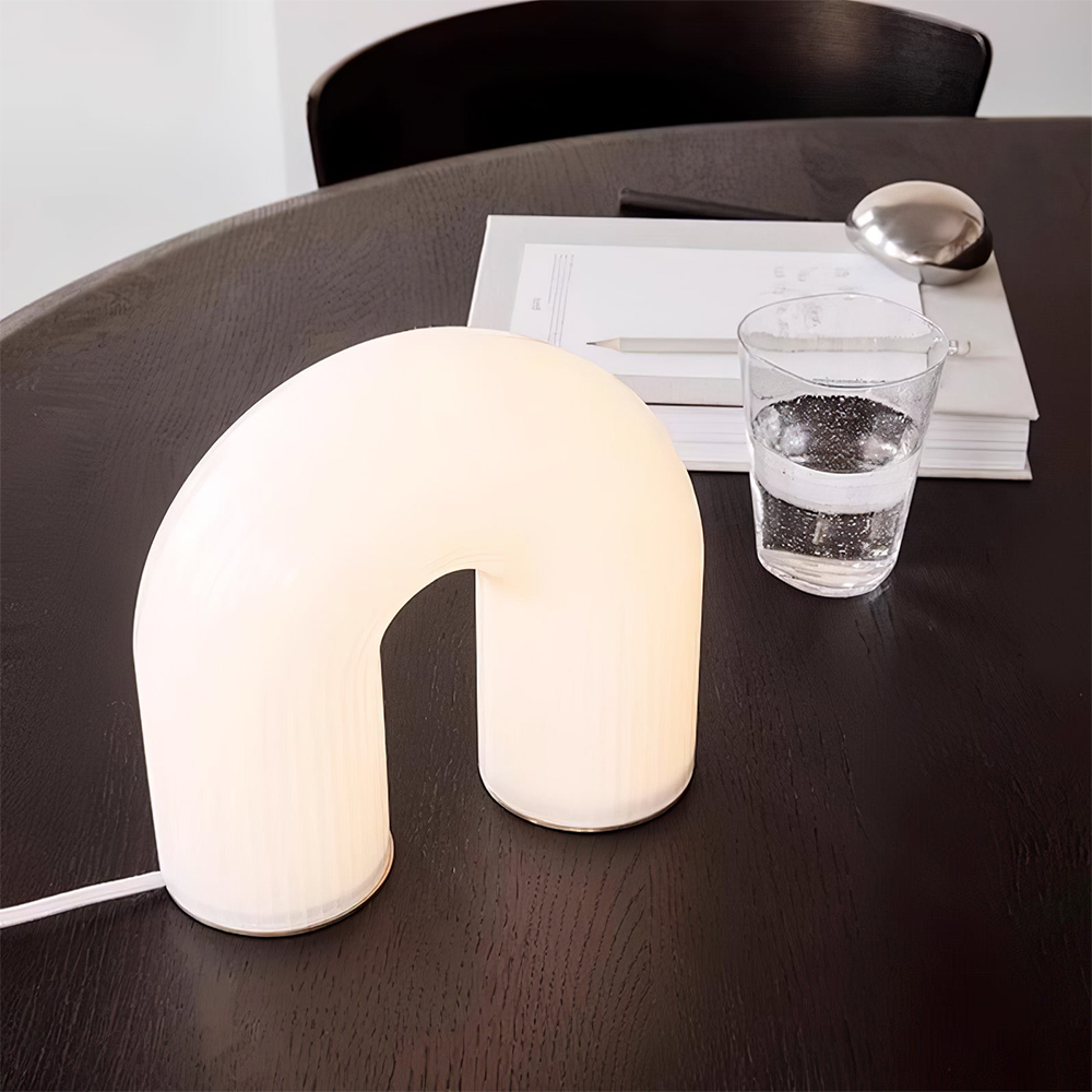 High angled view of the Arch lamp on a dark round wood table beside an open book, pencil and water glass